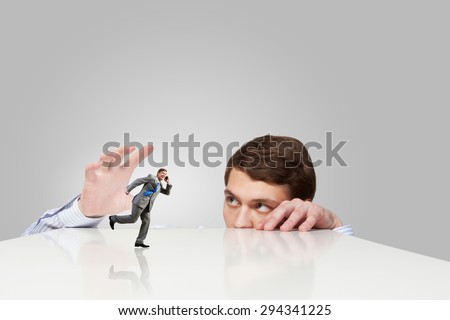 Young man looking from under table and catching running businessman