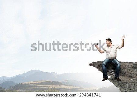 Fat man sitting on rock edge and screaming in megaphone