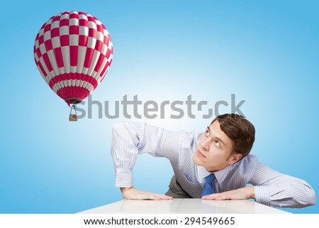 Young man looking from under table on flying balloon