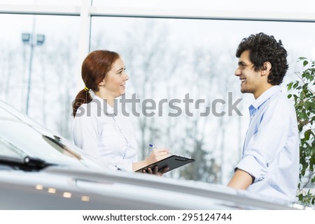 Young woman dealer in auto salon presenting car to customer