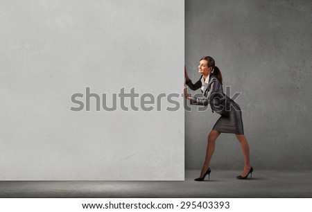 Young businesswoman making effort to move wall