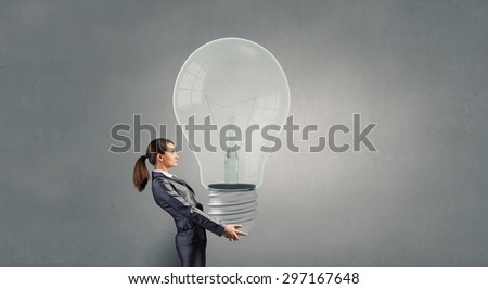 Young businesswoman carrying big light bulb in hands