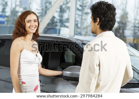Young man dealer in auto salon presenting car to customer