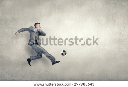 Businessman in suit jumping to hit soccer ball