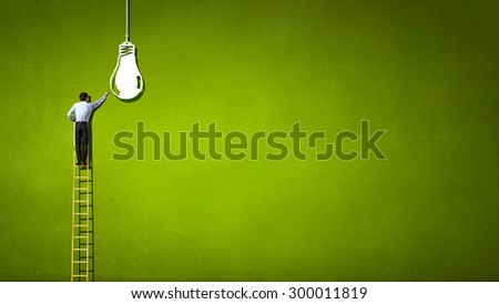 Back view of businessman standing on ladder and reaching light bulb