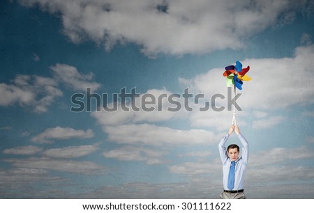 Young happy businessman flying in sky on colorful windmill