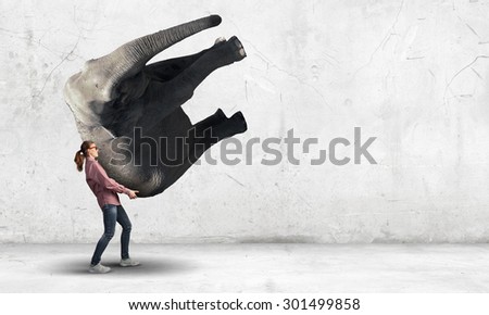 Funny young girl making effort to lift elephant