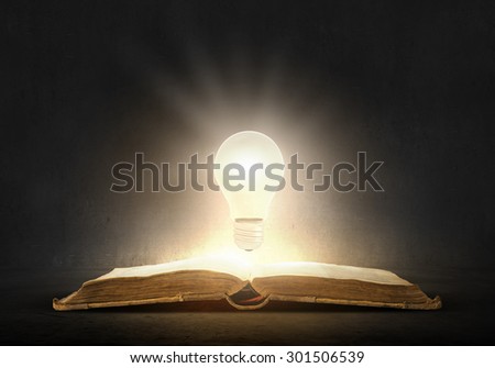 Old opened book and glowing light bulb