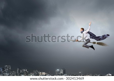 Young businessman flying on broom high in sky