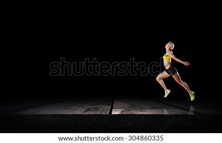 Young woman athlete running fast on dark background