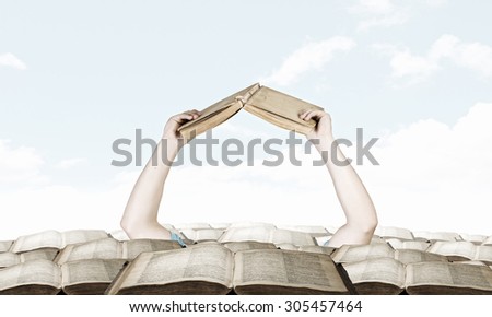 Hand with book reaching out from pile of old books