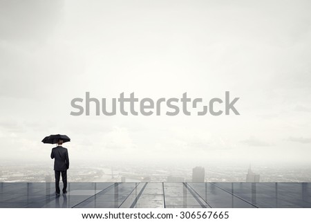 Back view of businessman with umbrella looking at city