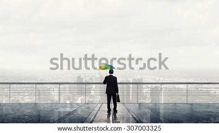 Businessman standing with back on building roof with colorful umbrella