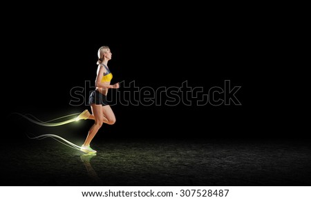 Young woman athlete running fast on dark background