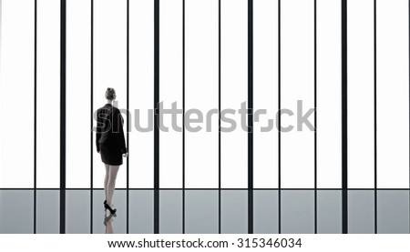 Businesswoman standing with back and looking in office window