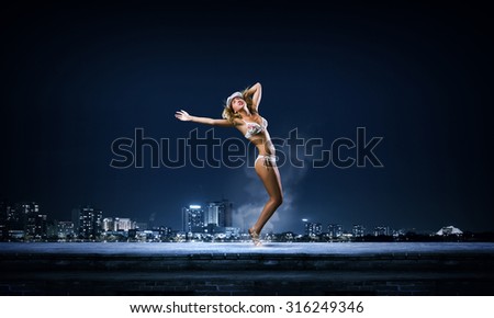 Hot young dancing woman in white bikini on night city background