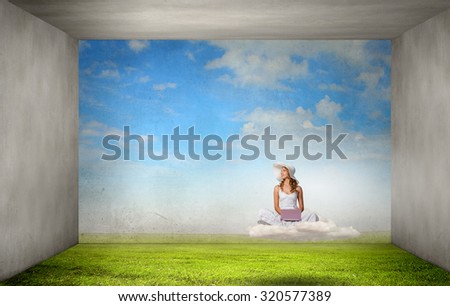 Young lady sitting on green grass with laptop on knees