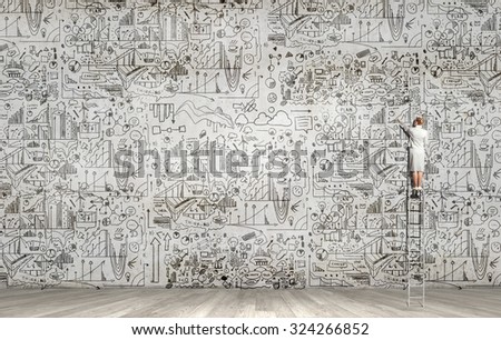 Rear view of woman standing on ladder and drawing science sketch on wall