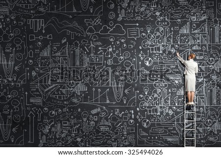 Rear view of woman standing on ladder and drawing science sketch on wall