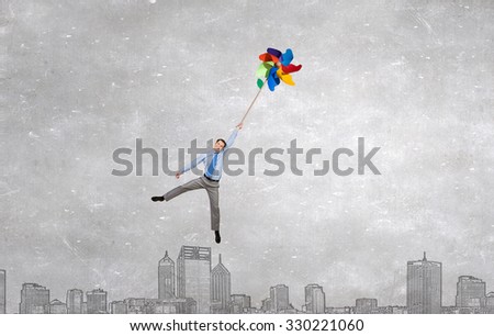 Young happy businessman flying in sky on colorful windmill