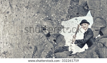 Young pretty woman in suit and hat crashing wall with baseball bat