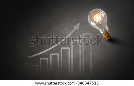 Glowing glass light bulb hanging from above and business sketches at dark background