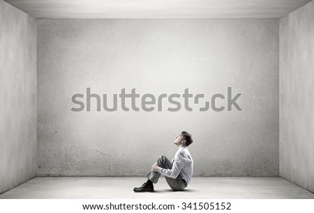 Young depressed businessman sitting on floor alone in empty room