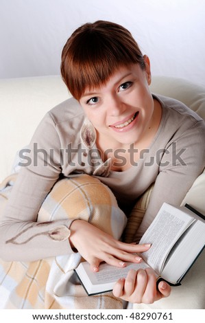 Young charming brunette in a gray jacket, reading a book sitting on the couch