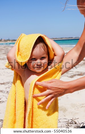 smiling little girl in a yellow towel on the beach. Caring mother\'s hands to help her.