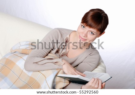 Young charming brunette in a gray jacket, reading a book sitting on the couch