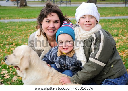 Mom and two sons together having fun in the autumn park playing with the dog