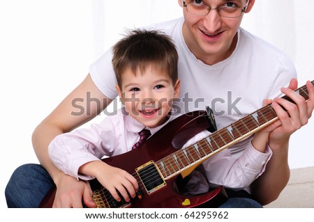 A young father teaches his young son to play guitar