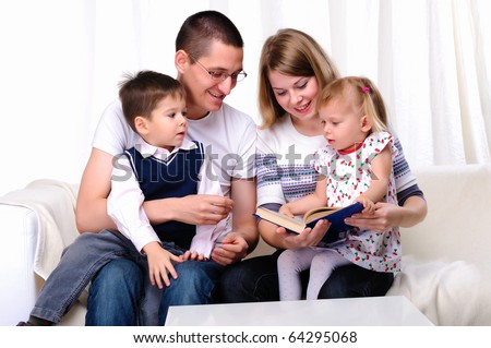 Mom, daughter, son and dad reading a book together on the couch
