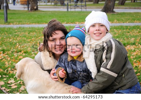 Mom and two sons together having fun in the autumn park playing with the dog