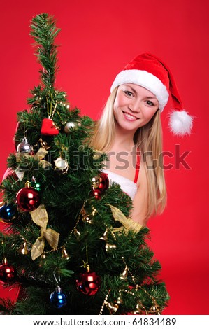 a young girl dressed as Santa Claus on a red background dresses up Christmas tree. Happy New Year and Merry Christmas!