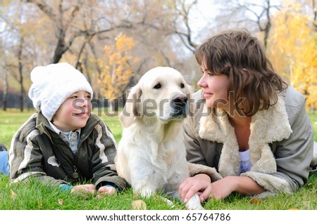 Mother and son together having fun in the autumn park playing with a golden retriever.