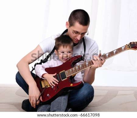 A young father teaches his young son to play guitar
