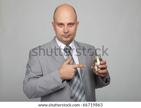 Bald businessman in a gray suit with a gray background with a can with coins in hand