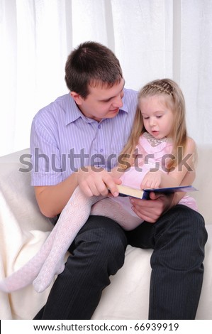The little girl is sitting on the lap of his father, and reads with him a book.