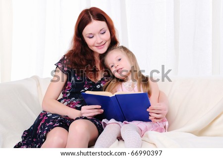 The little girl and her mother read a book together on the couch