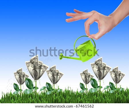 Hand with a small watering can watering green grass and shrubs of dollar bills