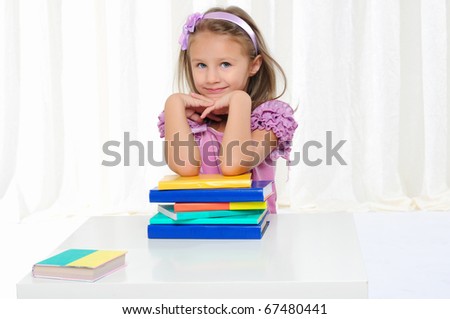 The little girl is studying literature. Reads a book while sitting at a white table.