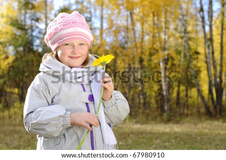 A little girl with a yellow flower in the autumn forest. Portrait.