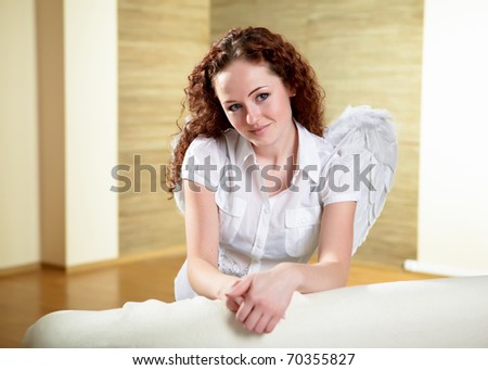 young red hair woman with angel wings sitting on a sofa