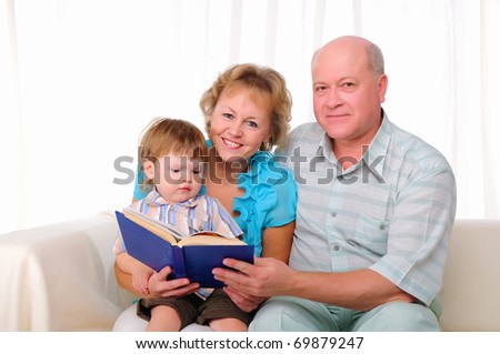 Grandmother, grandfather and grandson reading a book together. Symbol of the family.