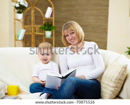 young mother reading a book to her little son at home