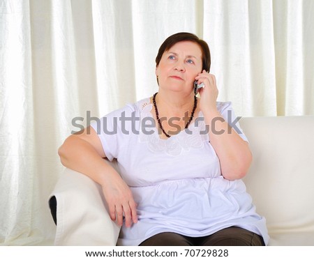 an old woman sitting on a sofa talking over mobile phone