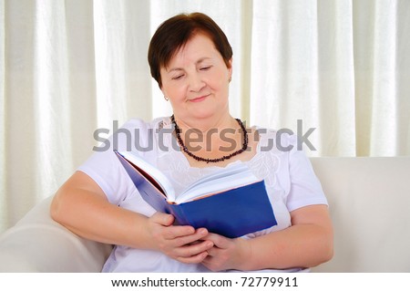 an old woman sitting on a sofa reading a book