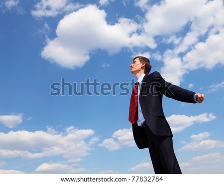young businessmanin a blue suit embracing air against blue sky
