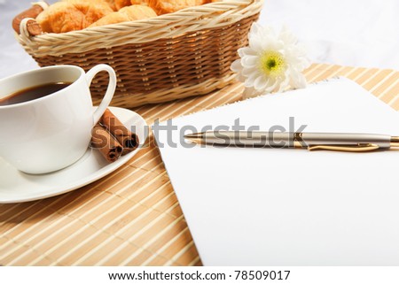 Breakfast coffee and croissants on a light background with a notebook for notes on the table.